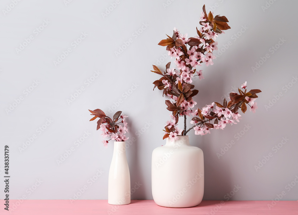 Vases with beautiful blossoming branches on table against light background
