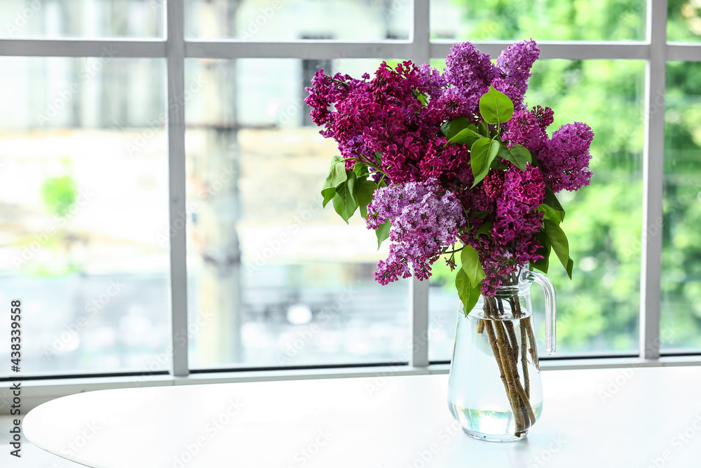 Vase with lilac flowers on table near window