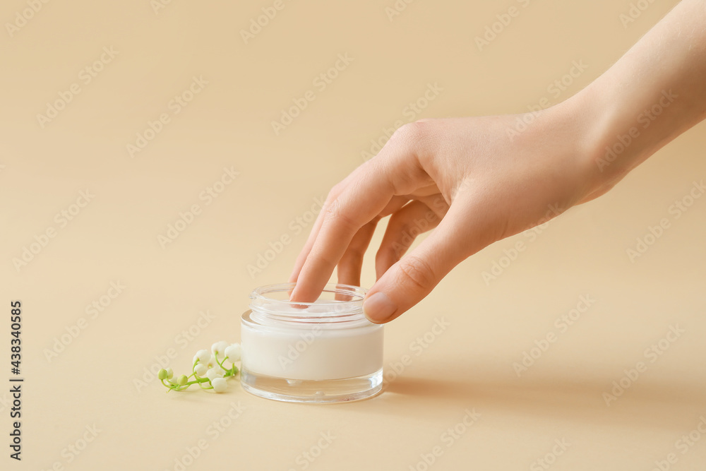 Female hand, jar of cream and lily-of-the-valley flowers on color background - obrazy, fototapety, plakaty 