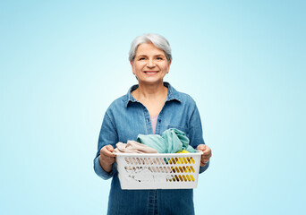 Poster - cleaning, wash and old people concept - portrait of smiling senior woman in denim shirt with towels in laundry basket over blue background