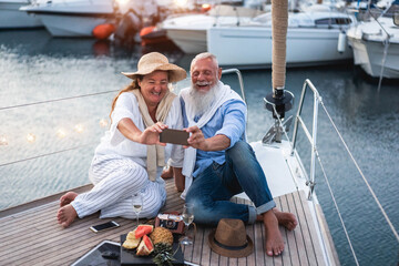 Wall Mural - Senior couple having fun doing selfie on sailboat during summer vacation - Travel and joyful elderly lifestyle - Main focus on senior man face