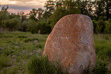 Fototapeta Desenie - Duży głaz narzutowy stojący pośród trawy na tle pomarańczowego zachodu słońca