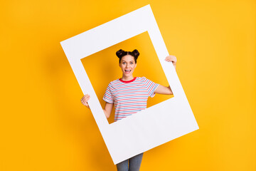 Sticker - Photo of childish sweet young girl dressed striped t-shirt holding big photo frame isolated yellow color background