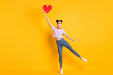 Sticker - Photo of excited charming young lady wear striped t-shirt holding big red heart isolated yellow color background