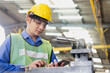 © Thirawatana - Manufacturing industry. Young male worker wearing hardhat and protection glasses with tablet look at machines in factory workshop.