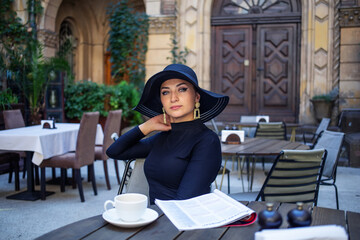 Exquisite woman in a black hat drinks coffee