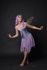 Canvas Print - Full length portrait of a purple haired  girl wearing fantasy corset dress with fairy wings and flower crown.  Standing pose against a dark studio background.