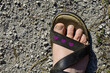 Frauenfuß in Sandale mit breiten Riemen, natürlich und ungepflegt unterwegs auf Kiesweg in der Sonne, Herzen in Rosa