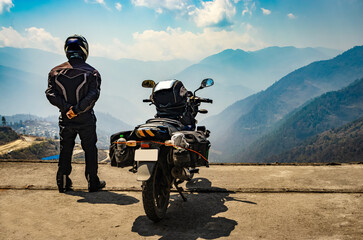 man motorcyclist watching valley from hill top with his loaded motorcycle and pristine natural view