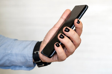 Close-up image of male hands using smartphone. searching or social networks concept, hipster man typing an sms message to his friends. Man painted nails. Design of male nails. men manicure.