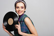 © LIGHTFIELD STUDIOS - joyful woman in headband holding retro vinyl disc isolated on grey.