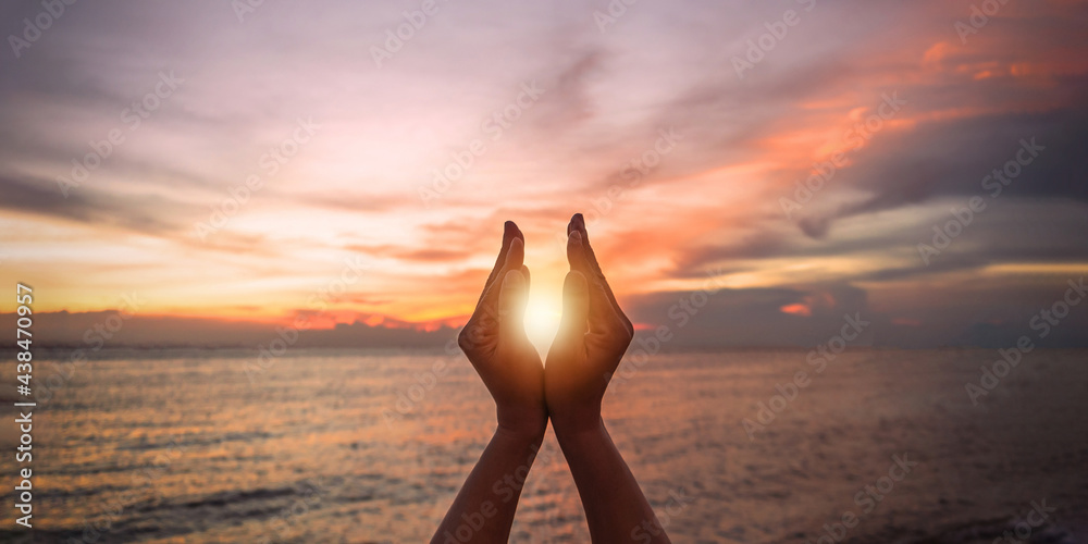 June summer solstice sun concept with silhouette of happy young woman's hands relaxing, meditating and holding sunset against warm golden hour sky on the beach with natural ocean or sea background - obrazy, fototapety, plakaty 
