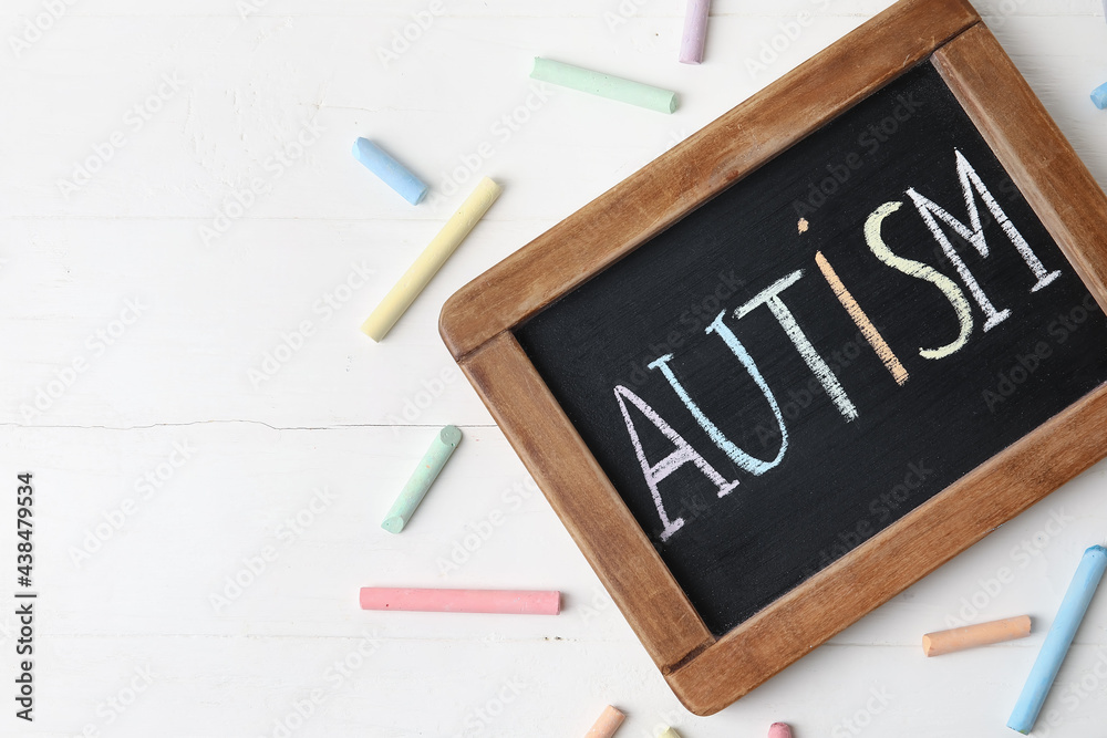 Chalk board with word AUTISM on white wooden background