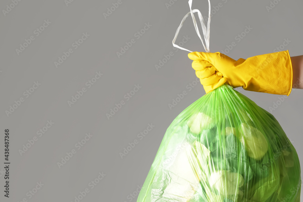 Woman holding bag with garbage on grey background, closeup