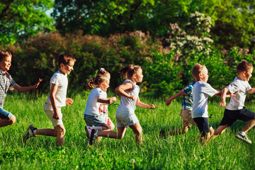 A group of happy children of boys and girls run in the Park on the grass on a Sunny summer day.