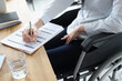 © H_Ko - Disabled woman in wheelchair filling out application for employment closeup