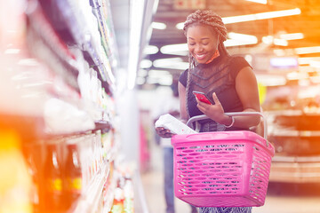 filtered image of excited african lady with shopping bag, smart phone in the hand in a shopping cent