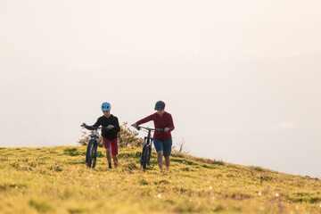 Wall Mural - Mother and daughter cycling uphill with mountain bikes at a sunset.