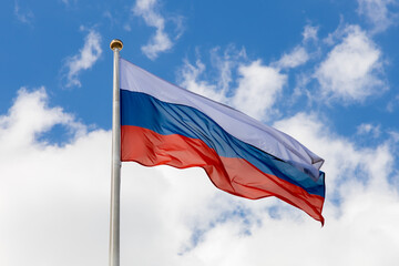 Wall Mural - Russian flag flutters in the wind, lower angle. The flag of the Russian Federation on a pole waving against a blue sky with clouds. Tricolor - state symbol of Russia