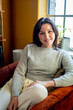 © Inti St. Clair - Portrait of smiling woman sitting in orange chair by window in home