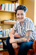 Portrait of smiling masculine looking woman in striped shirt sitting next to bookshelf