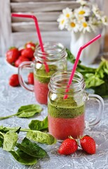 Wall Mural - Two-layered smoothies made of strawberries and spinach in a trendy jar with a handle. Next to fresh strawberries and juicy spinach leaves. organic food. For vegan and raw food nutrition. 