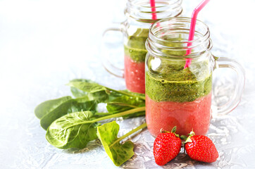 Wall Mural - Two-layered smoothies made of strawberries and spinach in a trendy jar with a handle. Next to fresh strawberries and juicy spinach leaves. organic food. For vegan and raw food nutrition. 