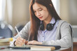 © EduLife Photos - Stock photo of a young teenage woman Asian college student in student uniform studying and writing on digital tablet in a university classroom