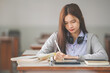 © EduLife Photos - Stock photo of a young teenage woman Asian college student in student uniform studying and writing on digital tablet in a university classroom