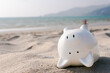 The supine piggy bank is facing financial problems from a business loss, at a sunburnt beach. In the background, the view of the blue sea.