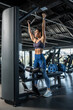© nazarovsergey - Young woman working out on lat pulldown machine at gym