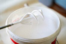 White Paint In Bucket With Work Tool Mixer On The Floor. Bucket With White Paint Indoors. Home Improvement Concept.