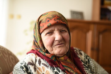 a very old woman in traditional Muslim clothes sitting in the house next to the window