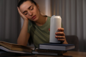 Poster - Tired young woman with energy drink studying at home, focus on hand