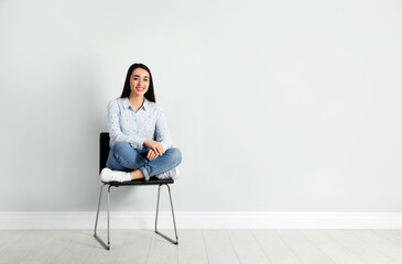 Wall Mural - Young woman sitting on chair near white wall in office, space for text