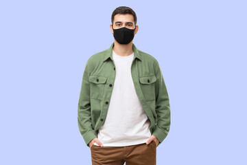 Young man wearing green workwear shirt and black cotton face mask, standing isolated on blue background