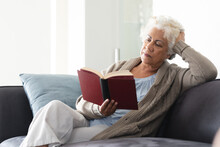 Mixed Race Senior Woman Sitting On Sofa Reading Book