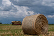A hay bale in the foreground with a trailer full of other bales in the background under a dramatic sky, Bientina, Pisa, Italy