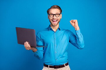 Photo of young business man happy positive smile use laptop rejoice victory fists hand isolated over blue color background