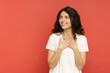Smiling young woman in oversize white t-shirt look excited to copy space for company promo. Portrait of pleased happy millennial female with curly brunette hair isolated over red studio background
