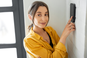 Cheerful woman enters a code on the alarm keyboard at the hallway indoors. Concept of home security and smart alarm