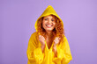 Redhead woman in yellow raincoat having fun isolated on purple background.