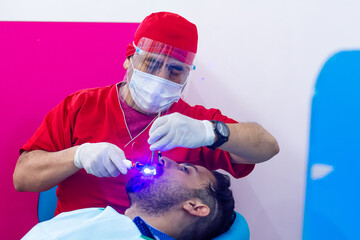 Dentist examining patient's teeth with ultraviolet lamp in a dental office