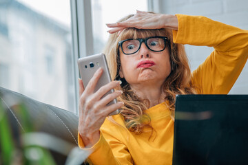stressed out woman looking at cell phone at home with computer
