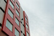 Commercial external metal composite panels on a building with blue sky and clouds in the background. The durable metal composite panels are both red and grey in color on the modern building.