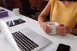 © wavebreak3 - Midsection of caucasian businesswoman sitting at desk using laptop and holding cup of coffee