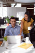 © wavebreak3 - Caucasian male and female colleague in discussion at desk looking at laptop and drinking coffee