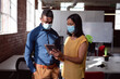 © wavebreak3 - Diverse male and female colleague wearing face masks standing in office looking at tablet together