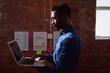 © wavebreak3 - Serious african american businessman standing in office holding and using laptop