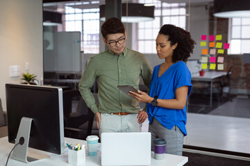 Diverse male and female colleague looking at tablet and discussing standing in office